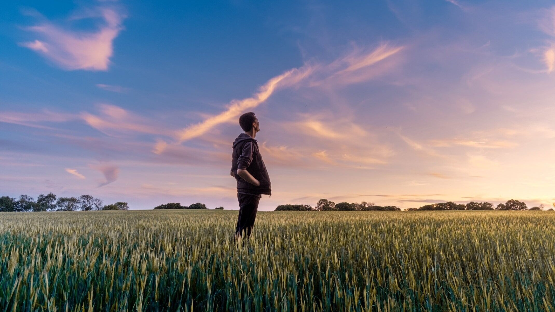 A man looking at the brightening sky as the sun rises slightly off camera